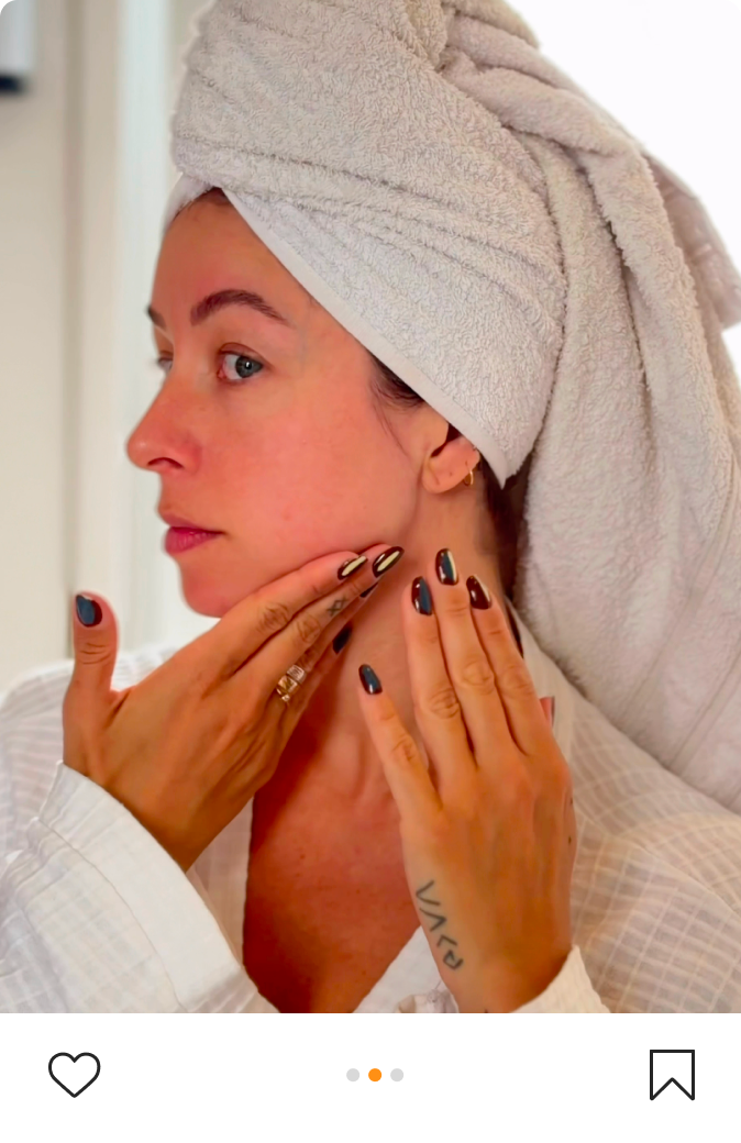 Girl with towel on her head delicately washes her face in mirror