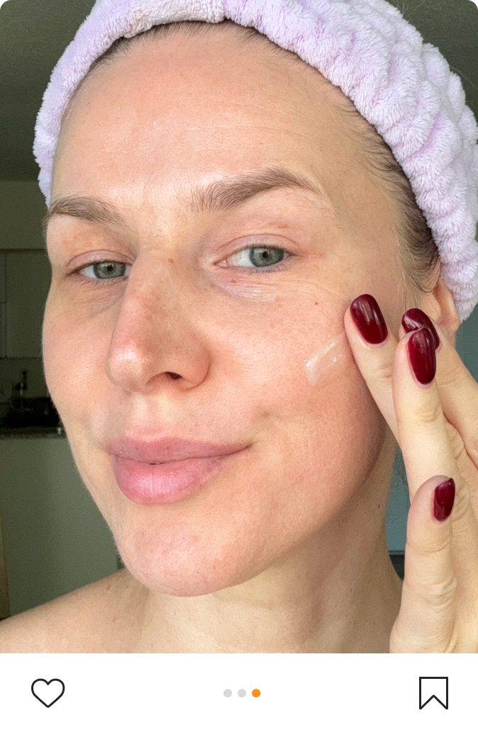 Girl with skincare headband smiles into camera while applying skincare cream to her face